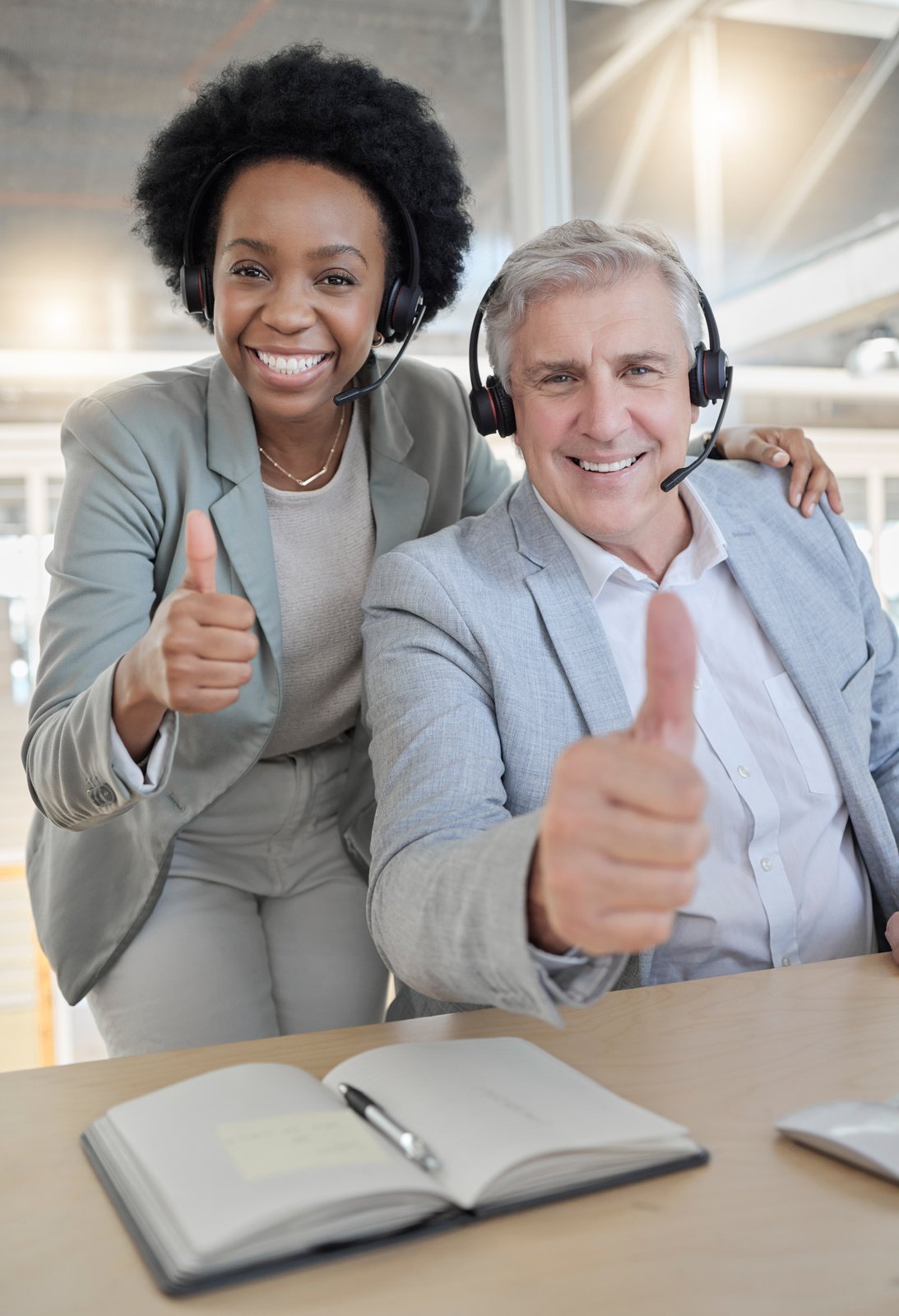 Customer support, thumbs up and portrait of black woman and man happy at desk in office. Contact us, help desk and teamwork with smile and notebook at advisory agency for crm training at call center.